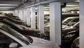 Ett svagt upplyst underjordiskt parkeringsgarage fyllt med parkerade bilar. Fordonen är placerade tätt intill varandra, med synliga pelare som stödjer taket. Scenen verkar organiserad och lugn.