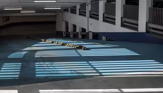 Ljus och skuggor skapar randiga mönster på golvet i ett tomt parkeringsgarage. Ett långt farthinder går över betongytan och utrymmet är upplyst av lysrör. Den övergripande tonen är cool och industriell.