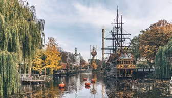 En vacker utsikt över en nöjesparksjö med ett dockat piratskepp. Flytande pumpor är i vattnet, omgivna av höstfärgade träd. I bakgrunden reser sig torn och attraktioner mot en molnig himmel.