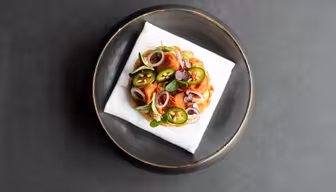 En pläterad maträtt med en välsmakande bakelse toppad med skivade jalapeños, lökringar och färska örter, serverad på en vit servett i ett runt, mörkt fat mot en mörk bakgrund.